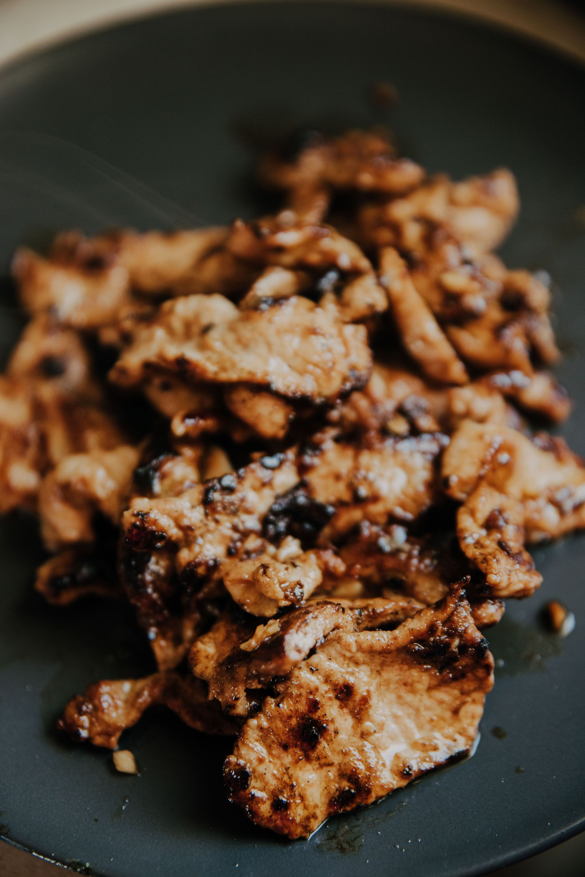 Close-up of savory grilled meat slices on a dark plate, showcasing delectable flavors.